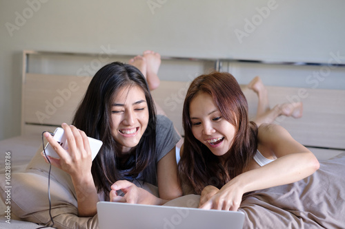 Girls friendship plan Hangout Traveling Holiday funny trip for this summer, checking popular places on laptop and smartphone on their bed