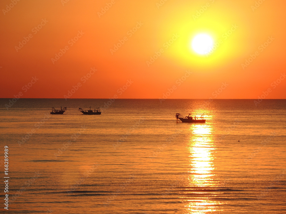 Fishing boats pull their nets at the sunrise. Adriatic cost. Emilia Romagna. Italy