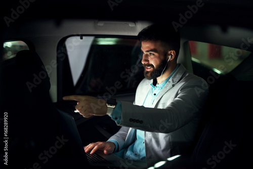 Elegant modern businessman with laptop on the back seat showing driver where to drive. © dusanpetkovic1