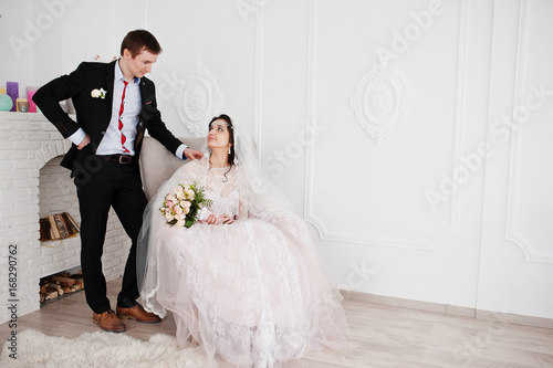 Groom standing next to the bride while she is sittin gon the chair with a bouquet in her hands.