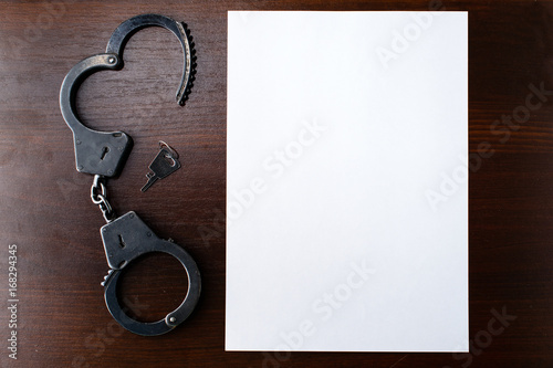 Fotografia steel police handcuffs and empty sheet of paper – frame for your text; top view