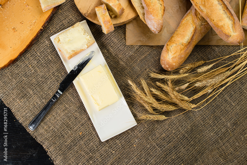 still life with French fresh bread baguettes with poolish on a wooden cutting board, butter and wheat. Shallow dof, flat lay still life with French fresh bread baguettes with poolish on a wooden cutting board, butter and wheat. Shallow dof, flat lay