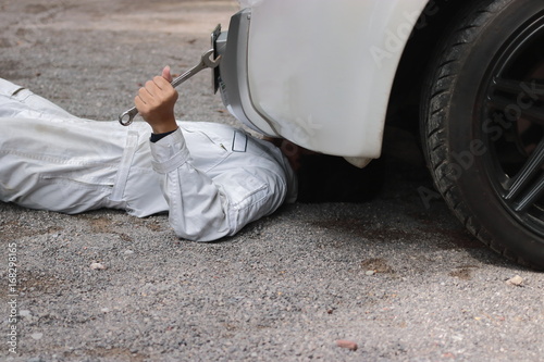 Side view of mechanic in white uniform lying down and fixing under car. Auto repair service.