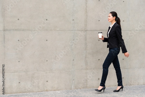 elegant manager woman walking on gray wall © PR Image Factory
