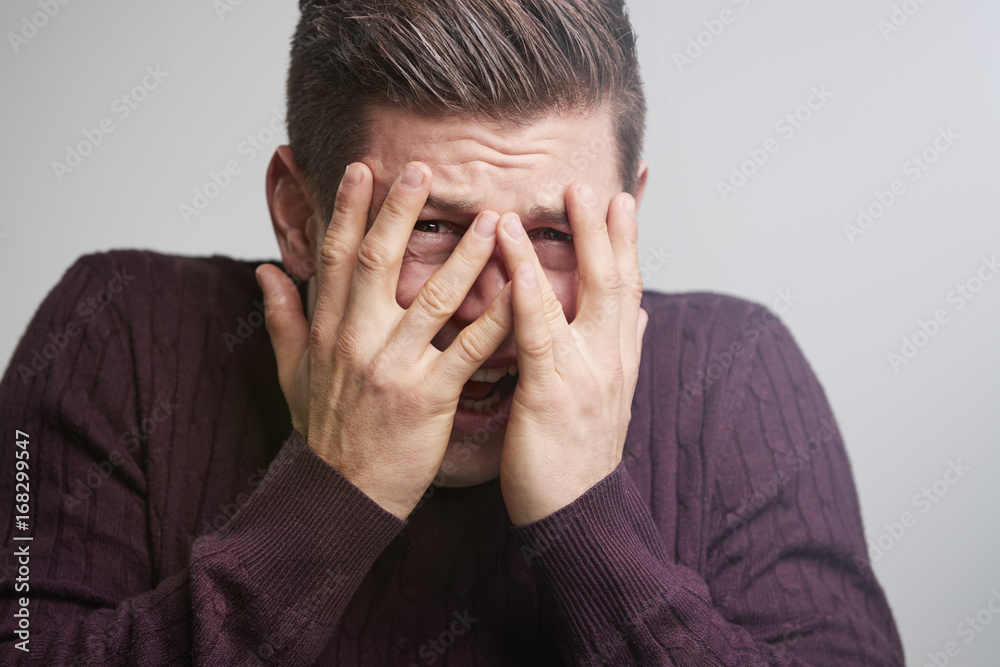 Scared young white man looking through his fingers Scared young white man looking through his fingers