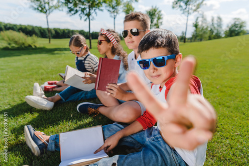 Multiethnic kids in sunglasses reading books and one boy gesturing at camera