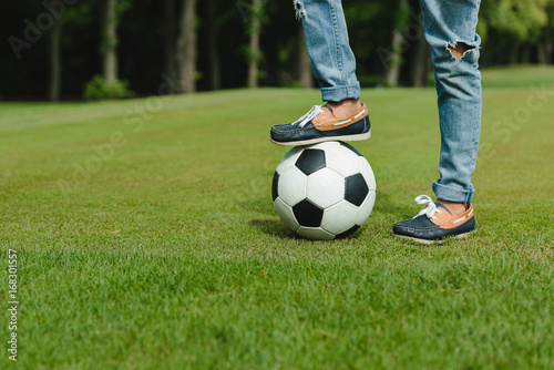 Close-up partial view of kid standing with soccer ball on green meadow © LIGHTFIELD STUDIOS