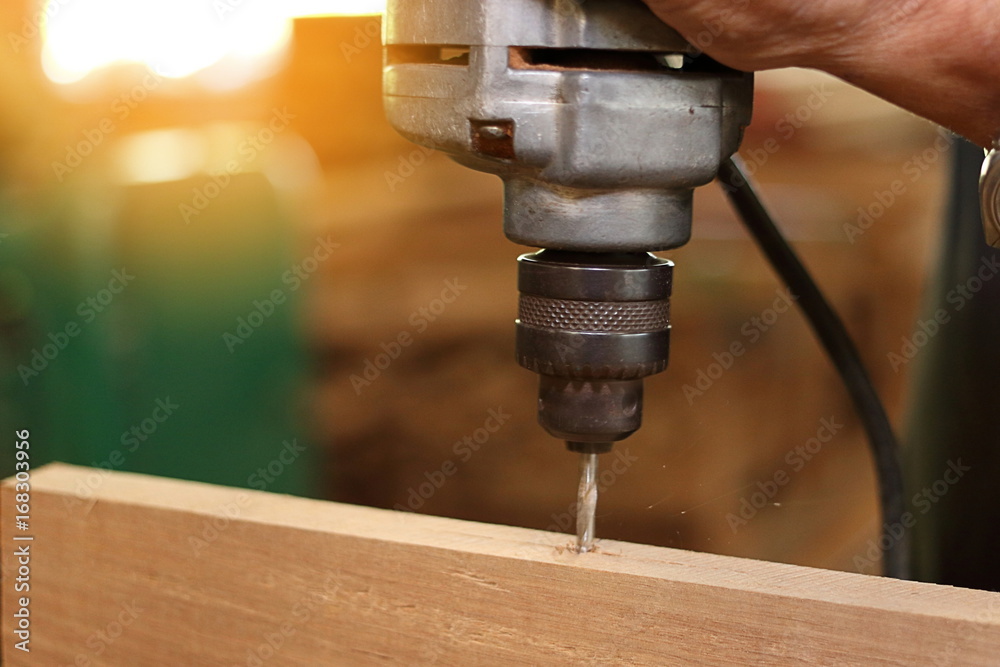 Close up electric drill is being worked with wooden board by worker. Selective focus and shallow depth of field.