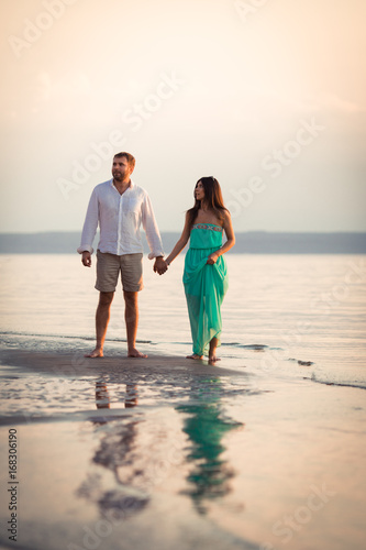 Husband and wife running along the river bank barefoot, a woman holding a dress