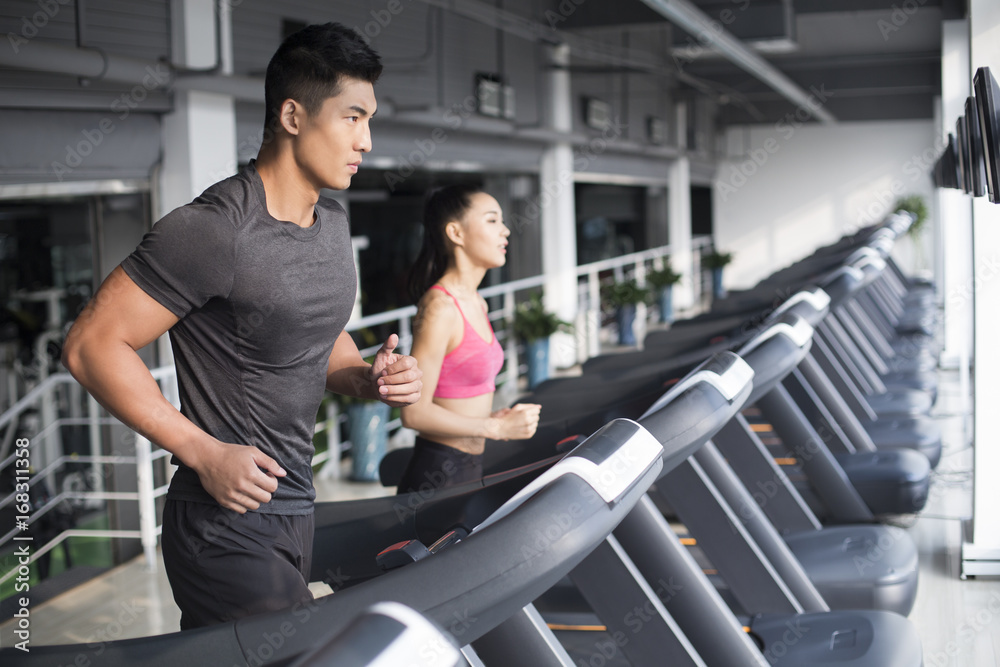 Young couple running on treadmills in gym Young couple running on treadmills in gym