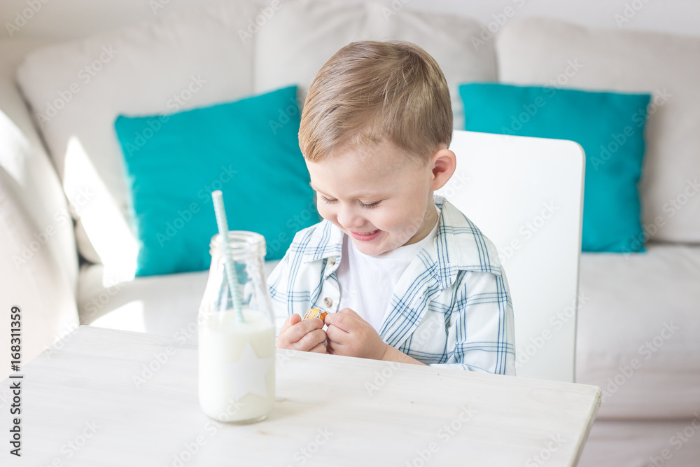 A cute little boy is eating candy and drinking milk. Health. Happy child. Breakfast. A little boy is sitting at the table. A cute little boy is eating candy and drinking milk. Health. Happy child. Breakfast. A little boy is sitting at the table.