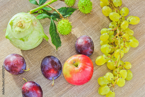 Autumn fruits, kohlrabi, chestnuts, apple, plum and grapes on wood background