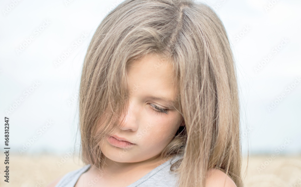 Portrait of adorable sad little girl with beautiful long hair on a summer day with blue sky and wheat field background Portrait of adorable sad little girl with beautiful long hair on a summer day with blue sky and wheat field background