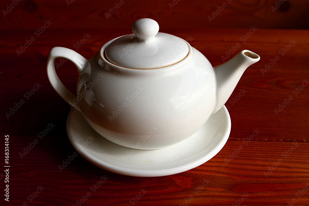 White teapot and the saucer on the wooden table alone White teapot and the saucer on the wooden table alone