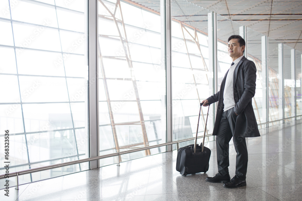 Businessman with wheeled luggage in airport lobby Businessman with wheeled luggage in airport lobby