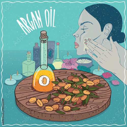 Glass Decanter of Argan oil and fruits of Argania spinosa plant. Girl applying facial mask on face. Natural vegetable oil used for skin care