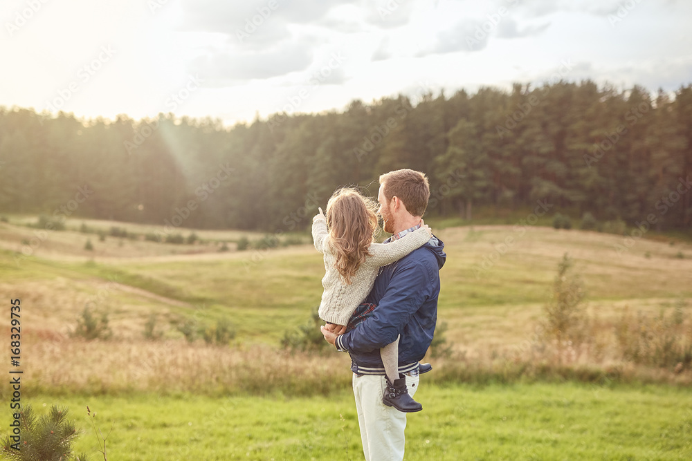 Little adorable girl being on his father s hands, pointing with her funger at big forest, wanting to go there. Father and daughter having walk on field, feeling relaxation, enjoying calm atmosphere