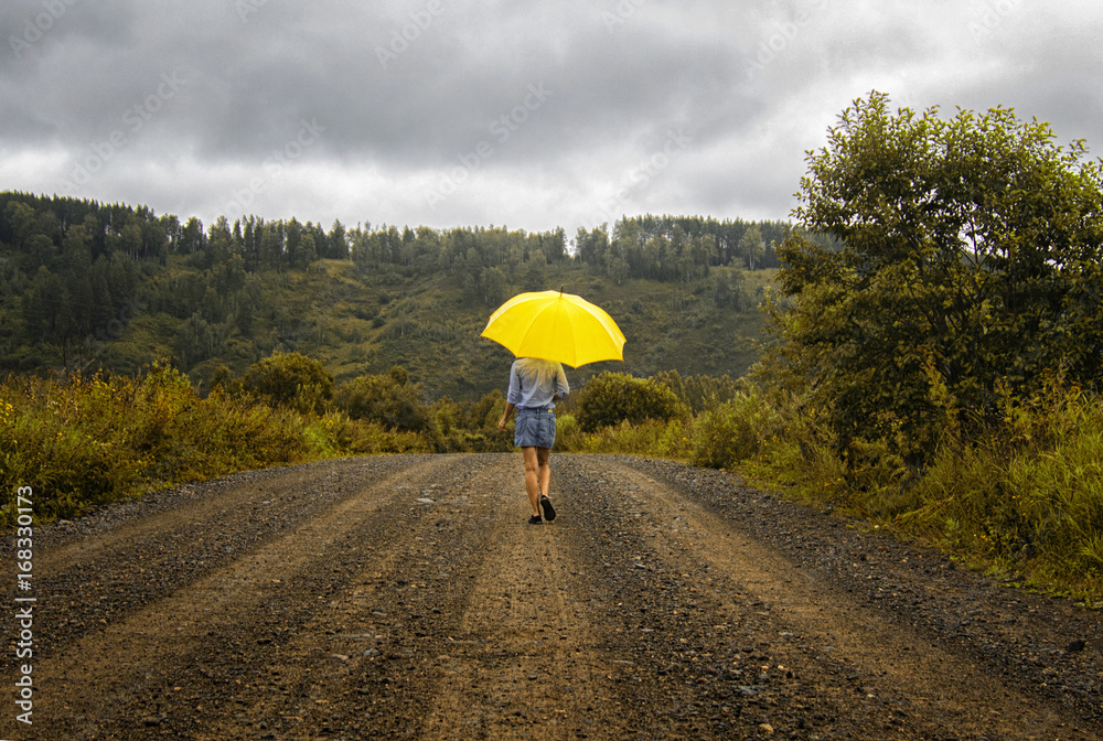 Beautiful woman hold yellow umbrella and walks on a country road under rain