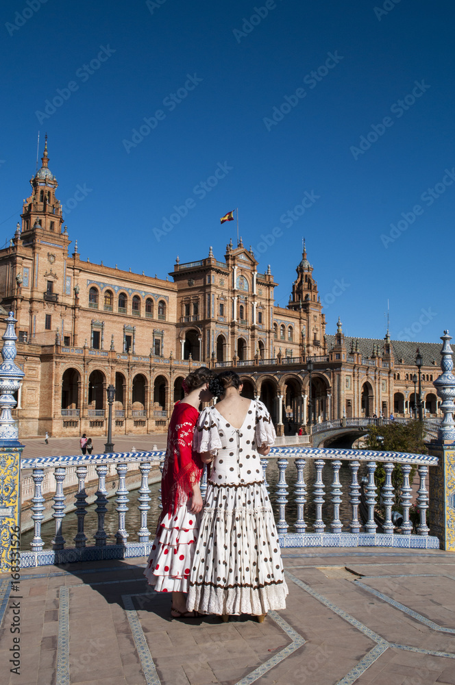 Fototapeta premium Spagna: ragazze sivigliane di spalle in abiti tipici in Plaza de Espana pronte per la Fiera di Siviglia (Feria de abril) che inizia due settimane dopo la Settimana Santa di Pasqua