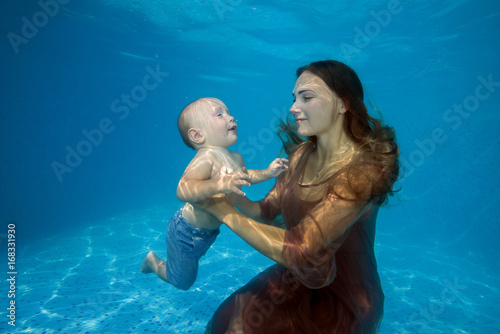 Obraz na plátně Woman in dress with little boy posing under water in pool