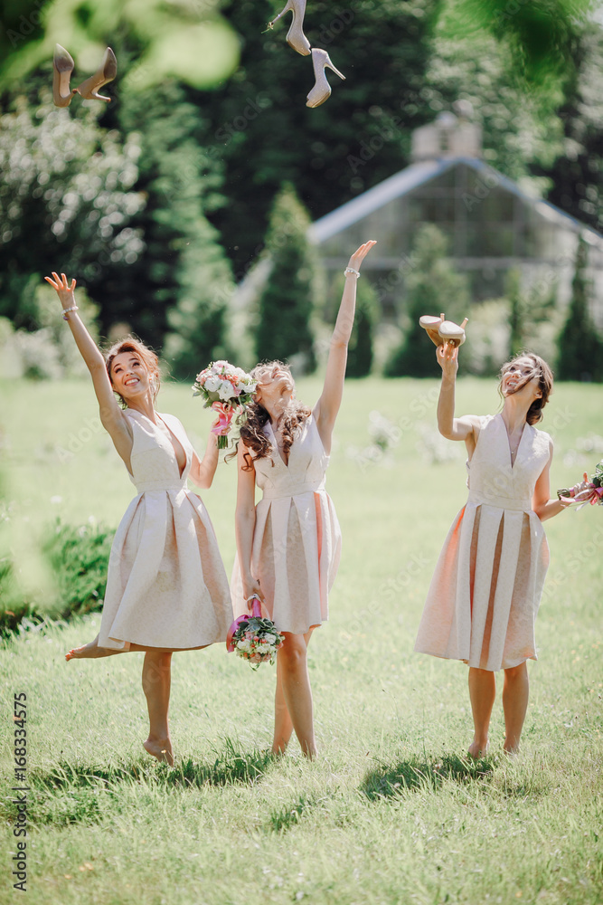 Beautiful bridesmaids in short dresses through their shoes up standing on the lawn Beautiful bridesmaids in short dresses through their shoes up standing on the lawn