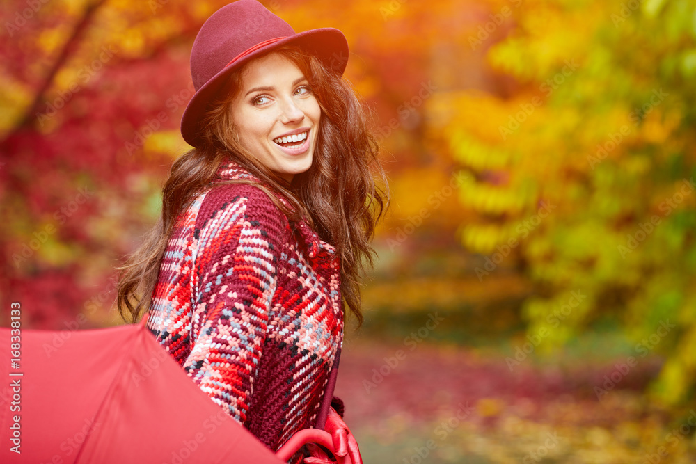Young woman with red umbrella walking on autumn city park. Beautiful fall time in nature