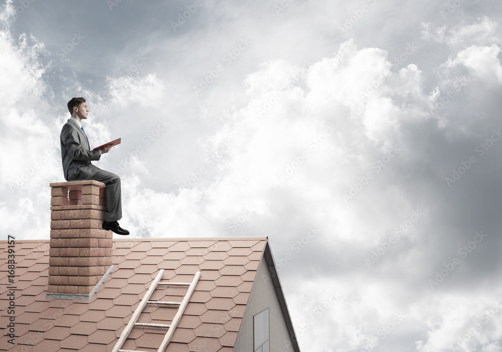 Student guy in suit on brick house roof reading book Student guy in suit on brick house roof reading book