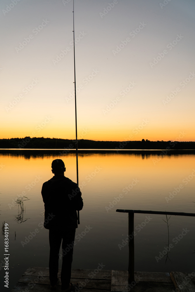 Silhouette fisherman at sunset. A man is fishing from the pier at sunset