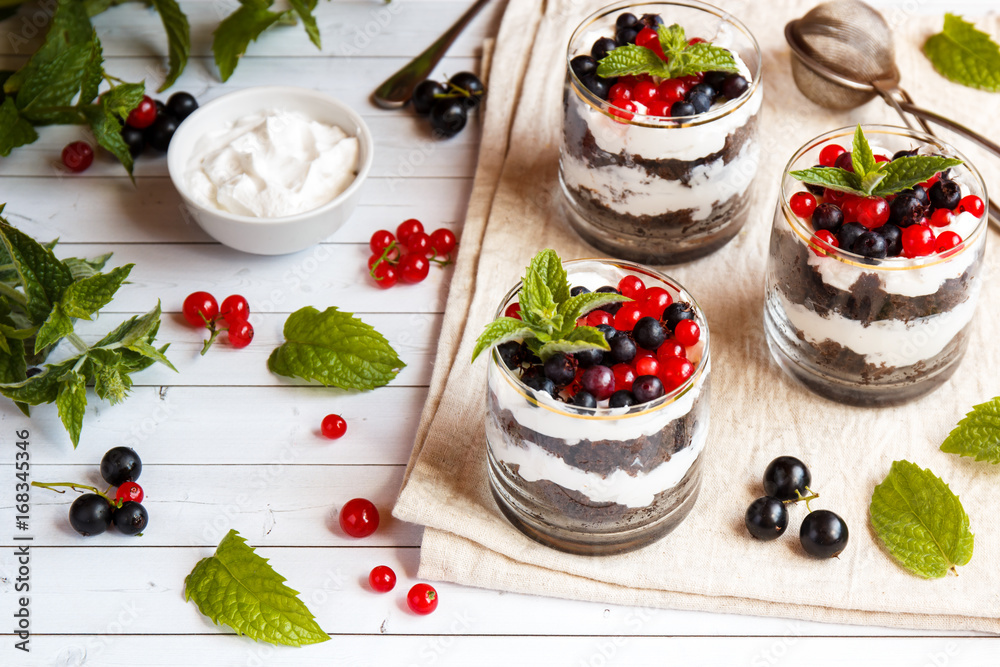 A sweet dessert of sponge cake with cream in a glass with fresh berries on wooden background A sweet dessert of sponge cake with cream in a glass with fresh berries on wooden background