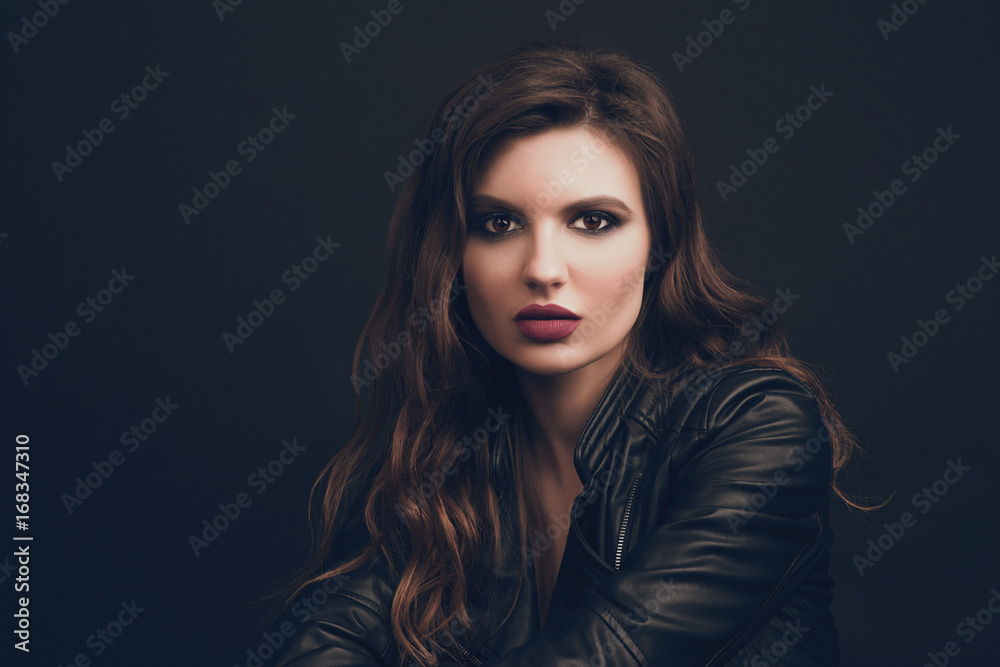 Portrait of the beautiful young woman with wavy brown hair posing at studio over black background. Toned. Portrait of the beautiful young woman with wavy brown hair posing at studio over black background. Toned.