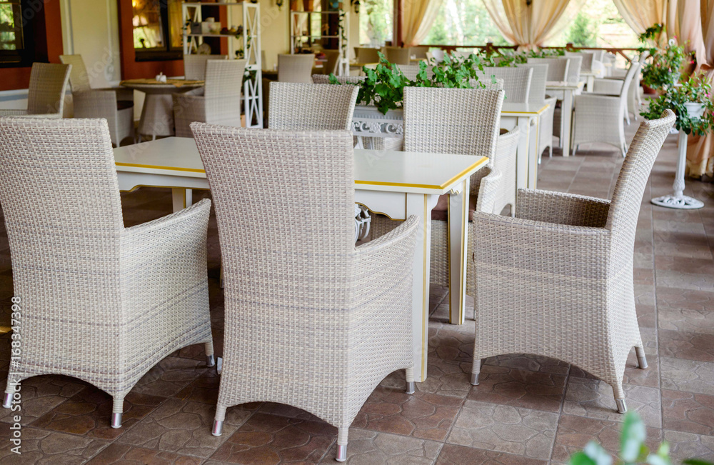Empty cafe with rattan wicker armchairs and tables on summer garden terrace outdoor, free space. Table and chairs in empty cafe. Wicker furniture rattan chairs on terrace Empty cafe with rattan wicker armchairs and tables on summer garden terrace outdoor, free space. Table and chairs in empty cafe. Wicker furniture rattan chairs on terrace
