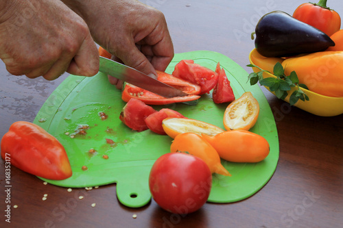 Male hands cutting ripe tomatoes and pappers into slices on cutting board. Close up. photo