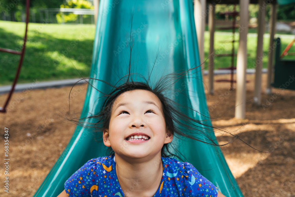 Young Asian American girl on playground slide with hair standing up