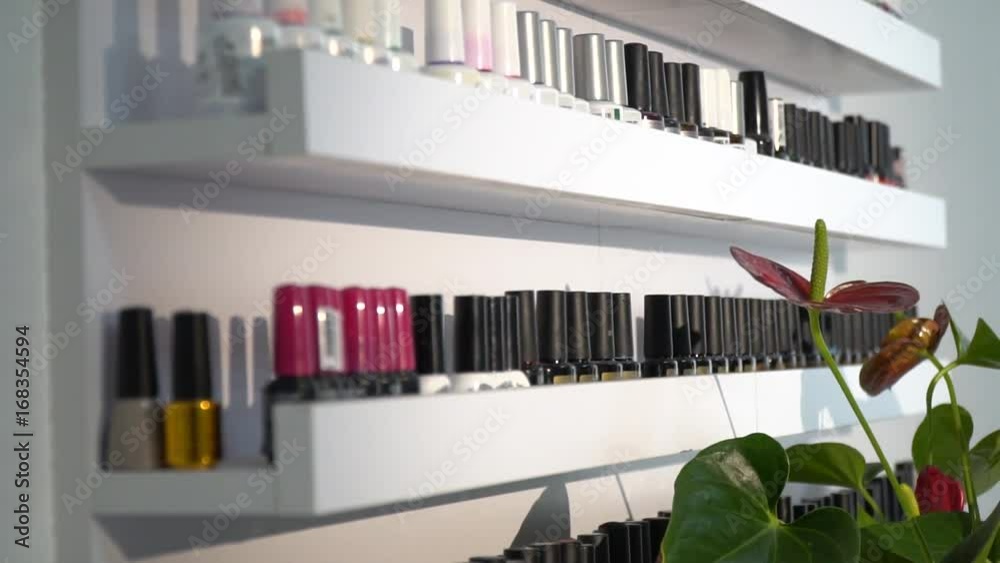 Multicolored bottles in nail polish stand on the shelves behind the flowers in the white room Multicolored bottles in nail polish stand on the shelves behind the flowers in the white room