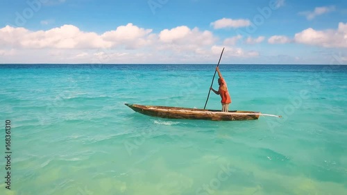 Aerial view of a poor fisherman with a torn shirt sails on a small boat on clear blue water along a tropical beach with beautiful hotels in Africa. Indian Ocean. Zanzibar. 2017