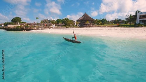 Aerial view of a poor fisherman with a torn shirt sails on a small boat on clear blue water along a tropical beach with beautiful hotels in Africa. Indian Ocean. Zanzibar. 2017