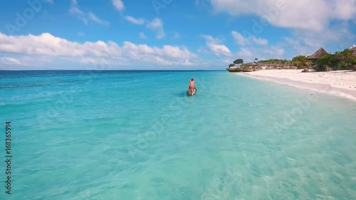 Aerial view of a poor fisherman with a torn shirt sails on a small boat on clear blue water along a tropical beach with beautiful hotels in Africa. Indian Ocean. Zanzibar. 2017
