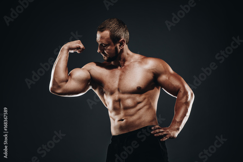 Strong athletic bodybuilder with muscular arm ands fist , perfect abs, shoulders, biceps, and triceps chest, personal fitness trainer flexing his muscles