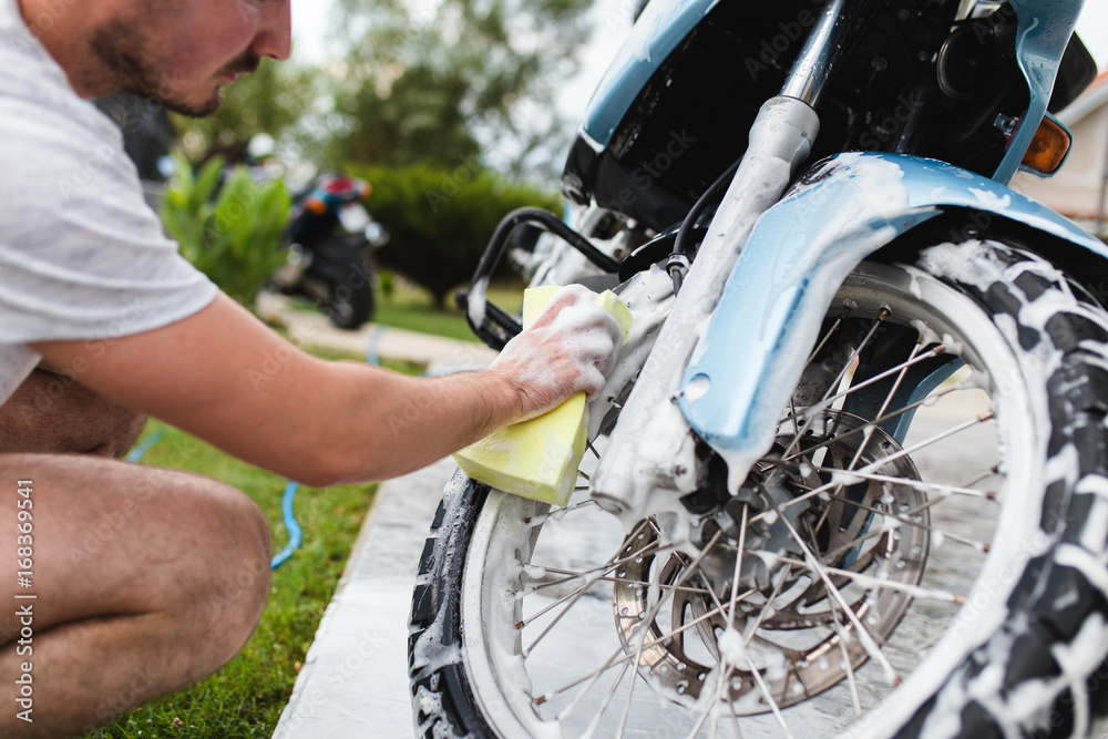 Obraz premium A man cleaning motorcycle with sponge, motorcycle detailing (or valeting) concept. Selective focus. 