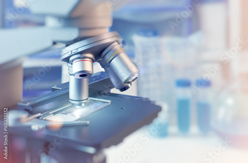 Scientific background with closeup on light microscope and blurred laboratory