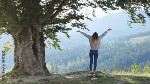 Young woman jumping mountain top back full view jump raised hands stretching having fun enjoying summer vacation cheerful freedom inspiration winning atmospheric wild nature place rejoice recreation