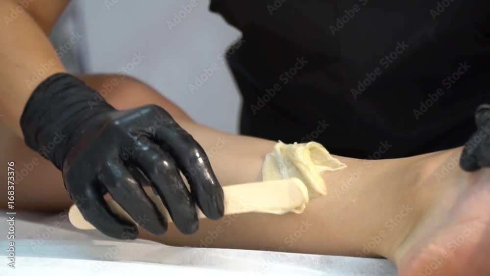Close up of the hands of a woman in black rubber gloves that rips off the sugary mass for epilation on slender female feet on white lounger, bit slow motion Close up of the hands of a woman in black rubber gloves that rips off the sugary mass for epilation on slender female feet on white lounger, bit slow motion
