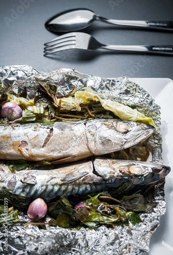 Steamed Saba fish with soy sauce and vegetable in foil on white plate