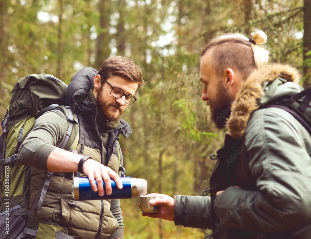 Camp, adventure, traveling and friendship concept. Man with a backpack and beard and his friend hiking in forest. Autumn color and hipster filter.
