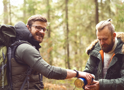Camp, adventure, traveling and friendship concept. Man with a backpack and beard and his friend hiking in forest. Autumn color and hipster filter. © Acronym