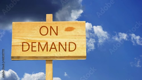 On demand words on a wooden sign against time lapse clouds in the blue sky photo
