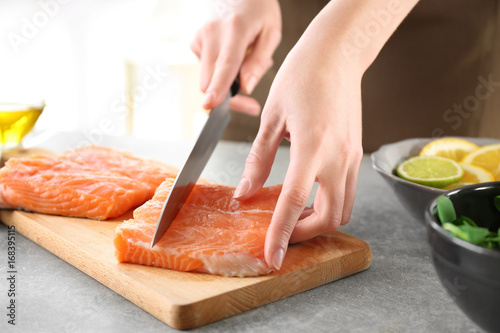Woman cutting fresh salmon fillet on wooden board