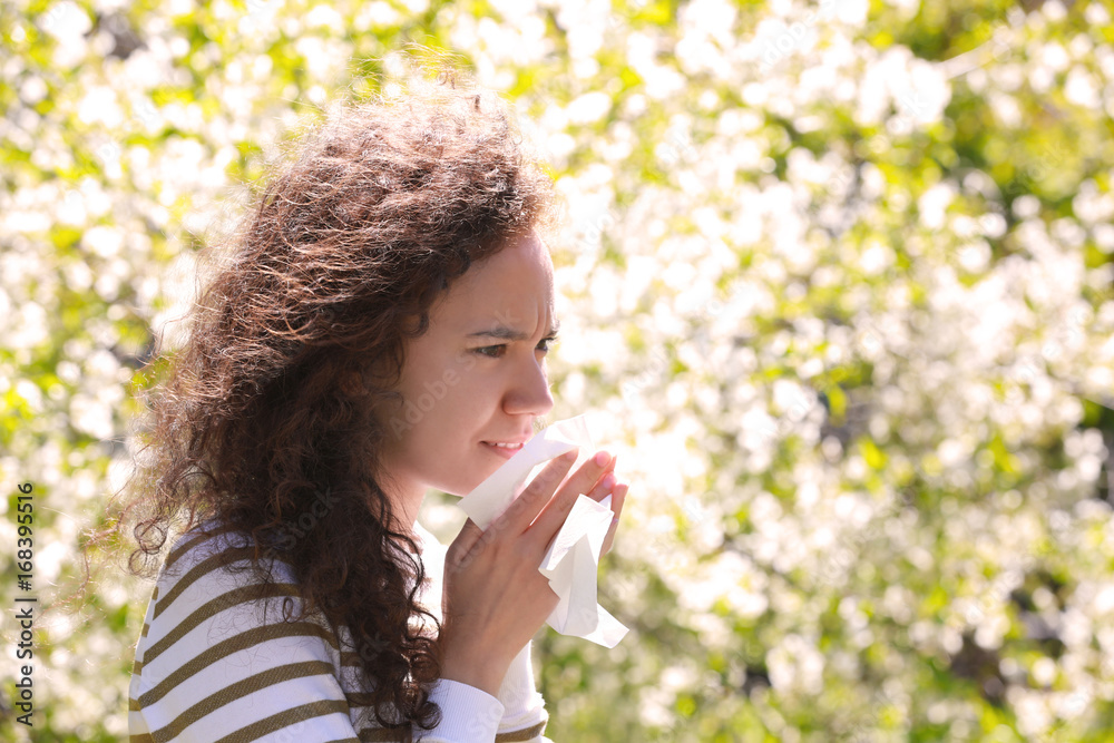 Allergy concept. Sneezing young girl with nose wiper among blooming trees in park Allergy concept. Sneezing young girl with nose wiper among blooming trees in park