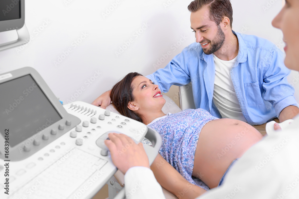 Young pregnant couple undergoing ultrasound scan in clinic Young pregnant couple undergoing ultrasound scan in clinic