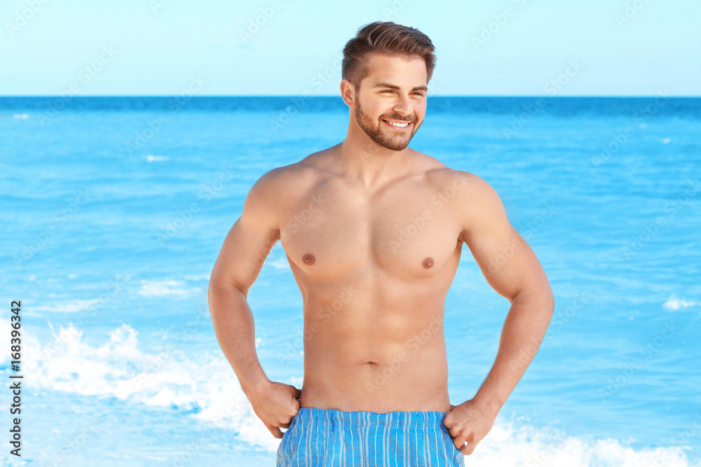 Handsome young muscular man in swimwear on sea background Handsome young muscular man in swimwear on sea background